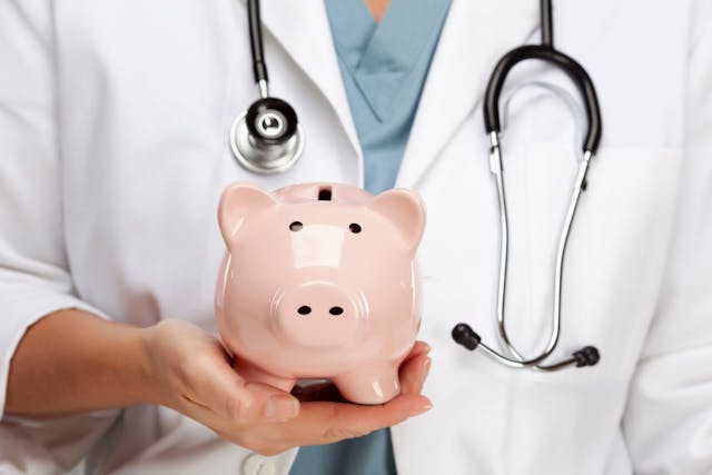 Doctor holding piggy bank | Image credit: Andy Dean – stock.adobe.com