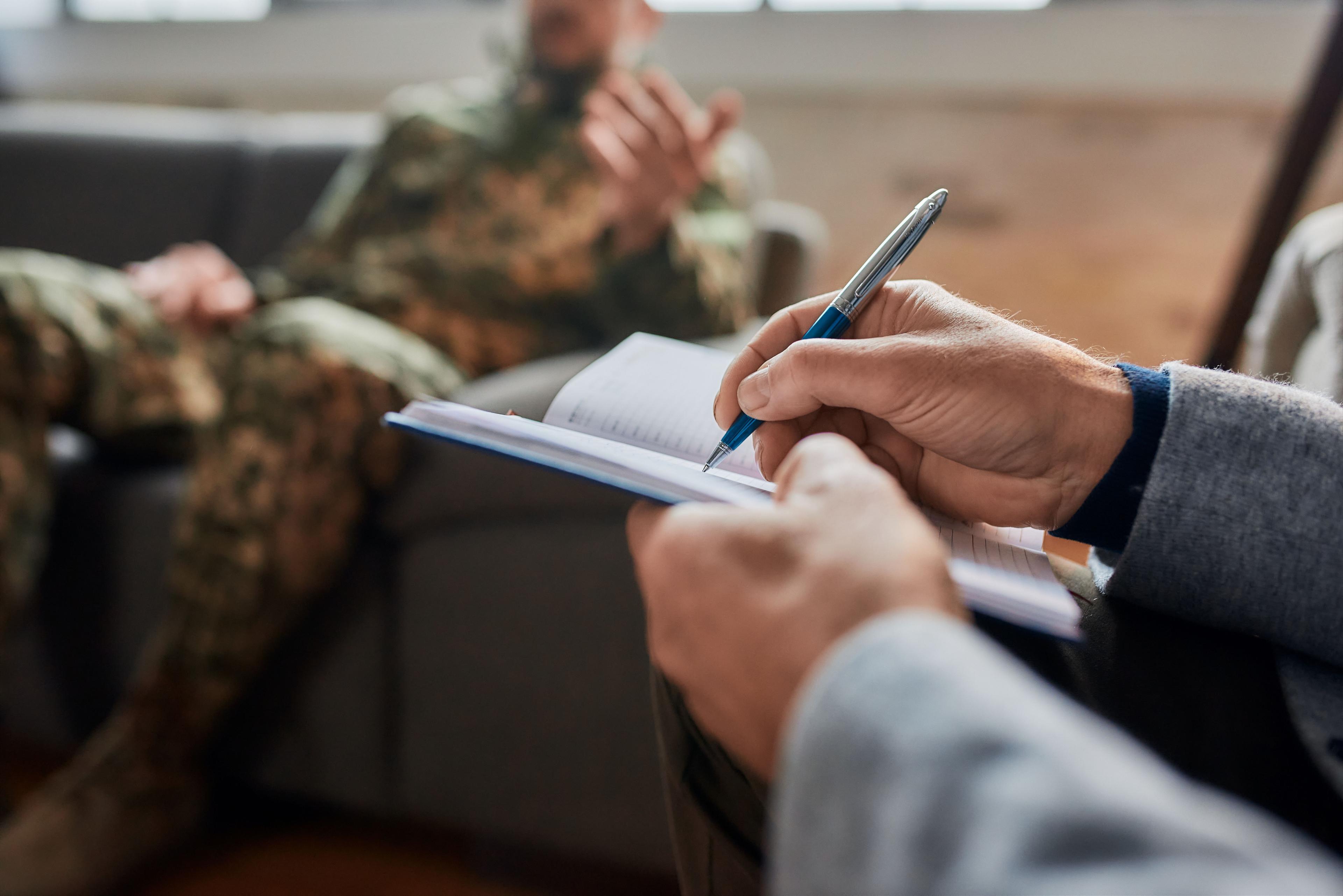 Notes. Close up of hands of psychologist making notes while communicating with military man during therapy session. Soldier suffering from depression - Svitlana - stock.adobe.com