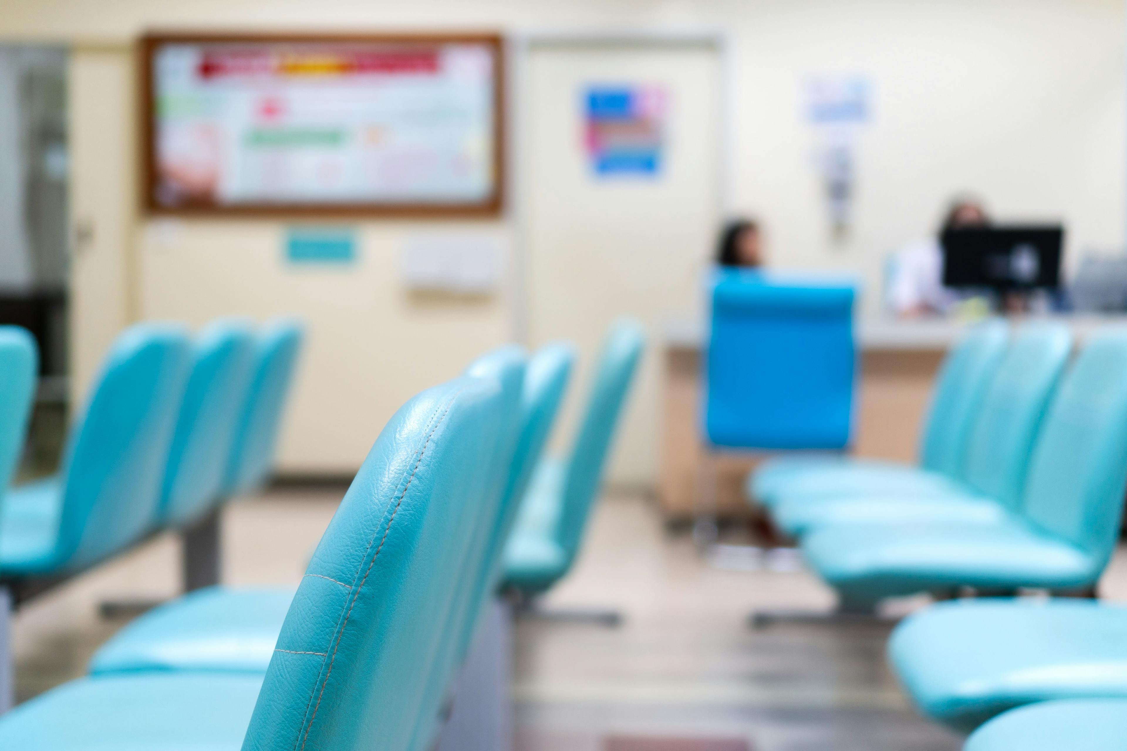 Empty blue chair in waiting room at hospital with blurred background of nurse desk - AePatt Journey - stock.adobe.com