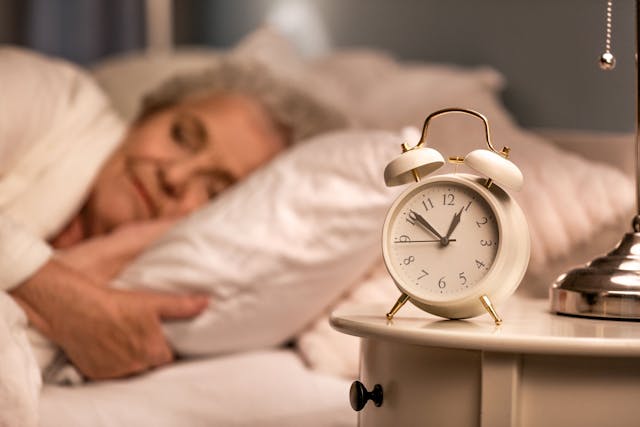Older woman sleeping with clock on nightstand | Image credit: Pixel-Shot – stock.adobe.com