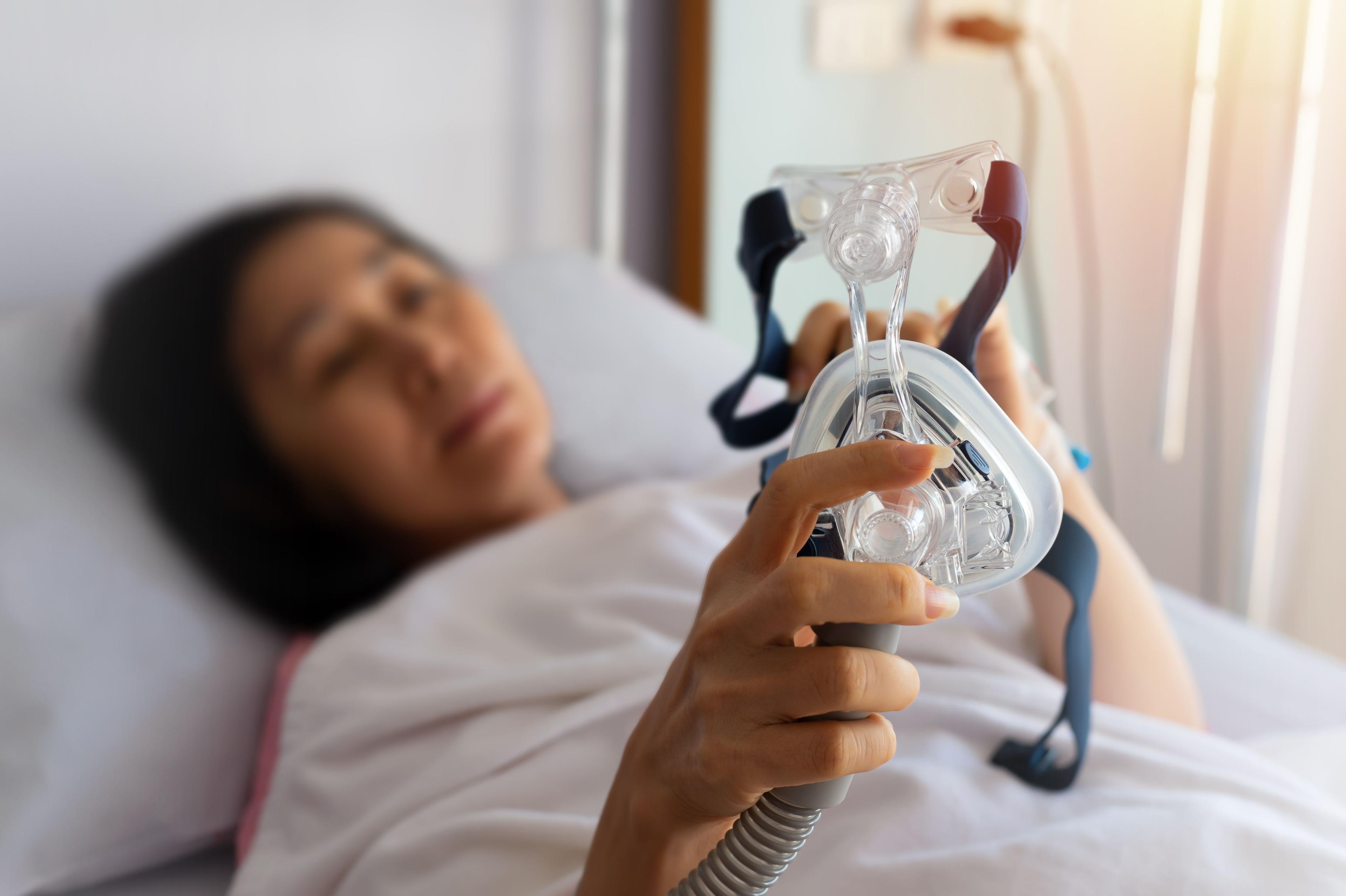 Woman in bed holding CPAP mask | Image credit: sbw19 – stock.adobe.com