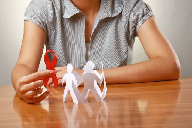 Woman holding HIV ribbon near paper people | Image credit: shefkate - adobe.stock.com