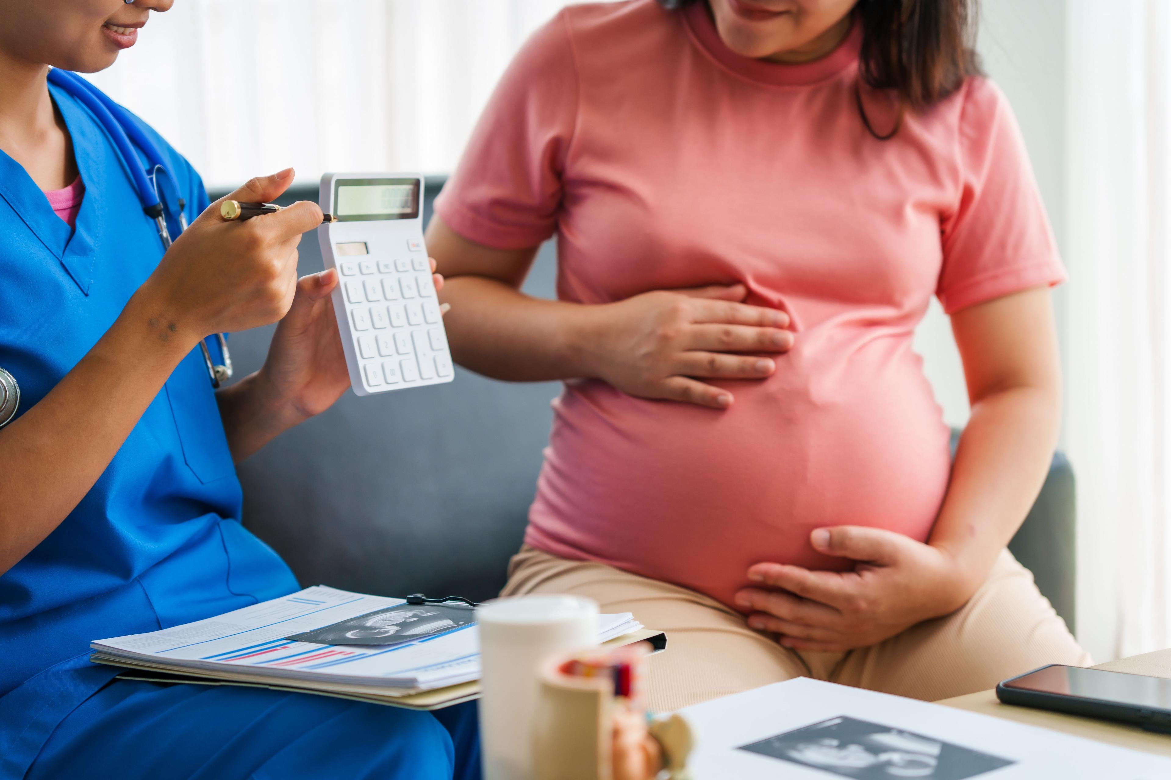 Health care provider helping pregnant woman calculate costs | Image credit: Phushutter – stock.adobe.com