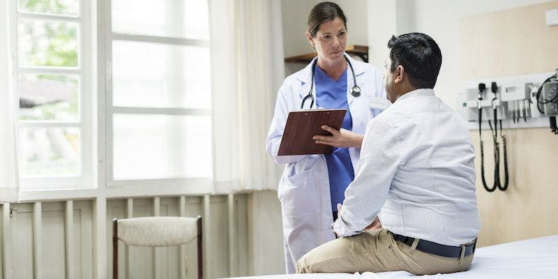 female doctor writing on a clipboard while speaking with a male patient