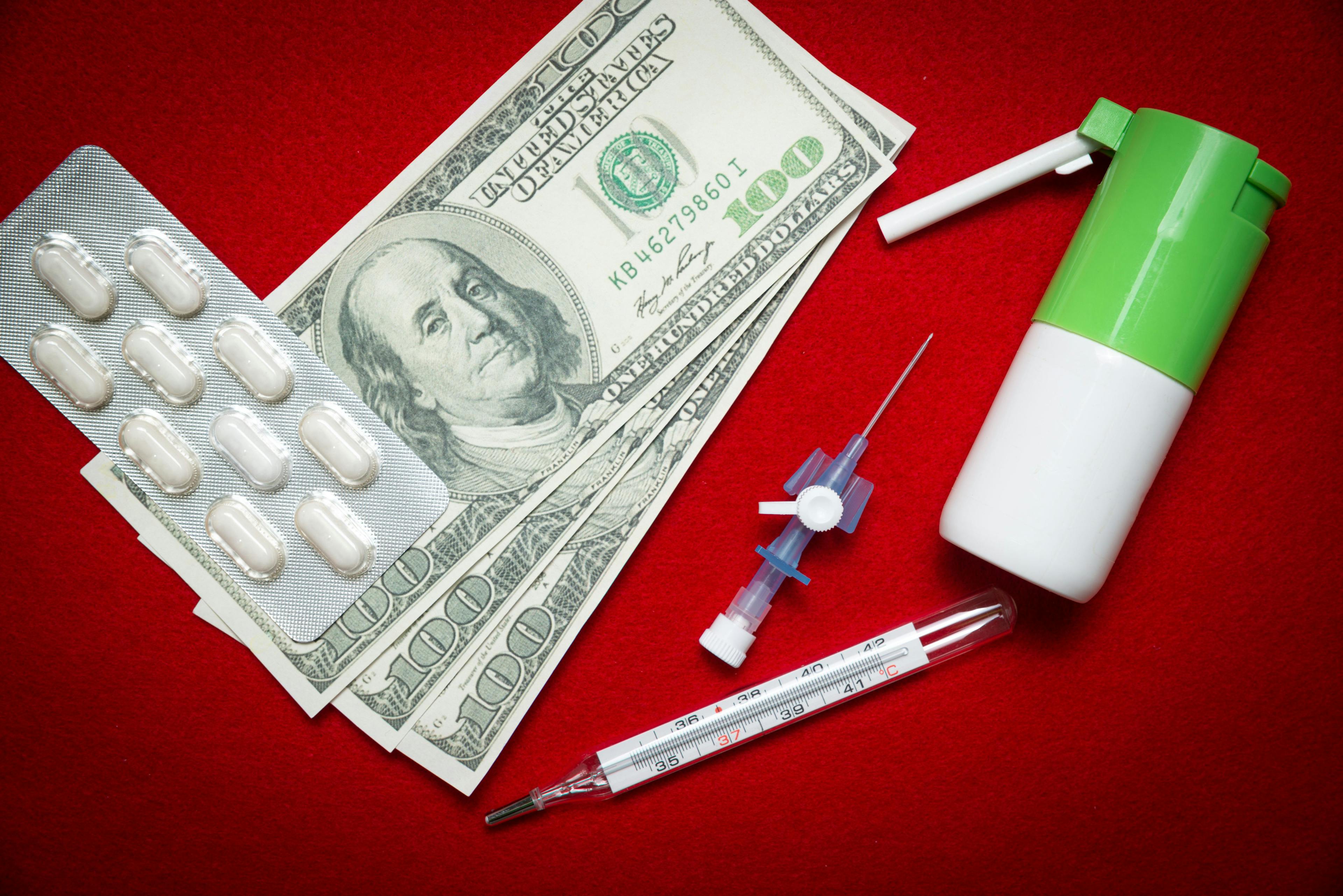 Pills, thermometer, inhaler and money on a red background | Sebastian - stock.adobe.com