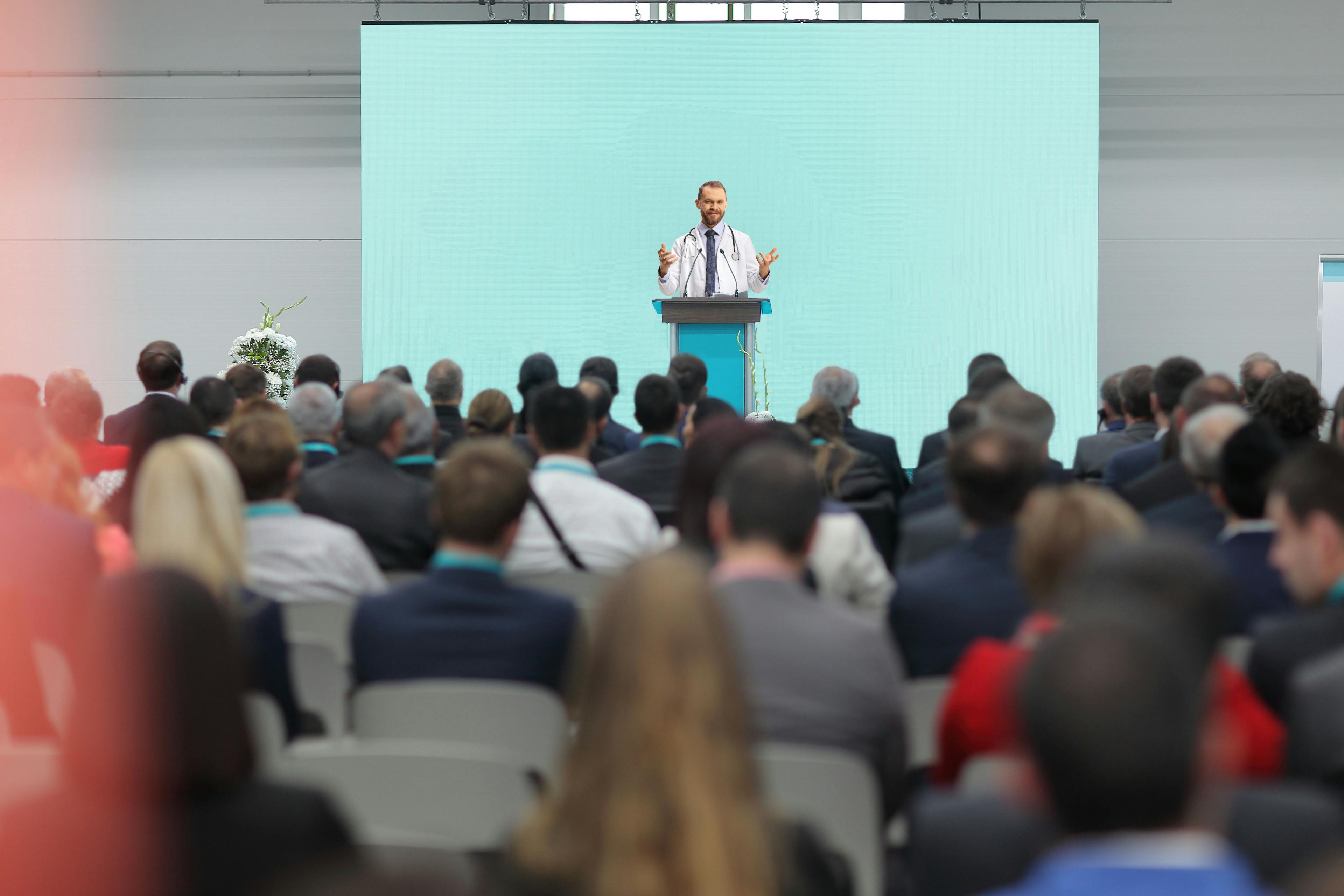 Male doctor giving a speech on a podium at a conference | Image credit: Ljupco Smokovski - stock.adobe.com