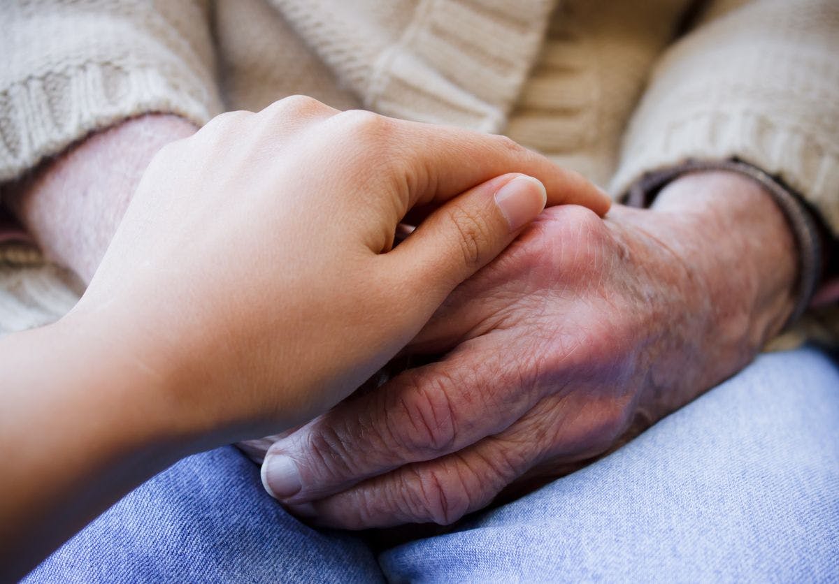 Young person comforting hands of elderly person.
