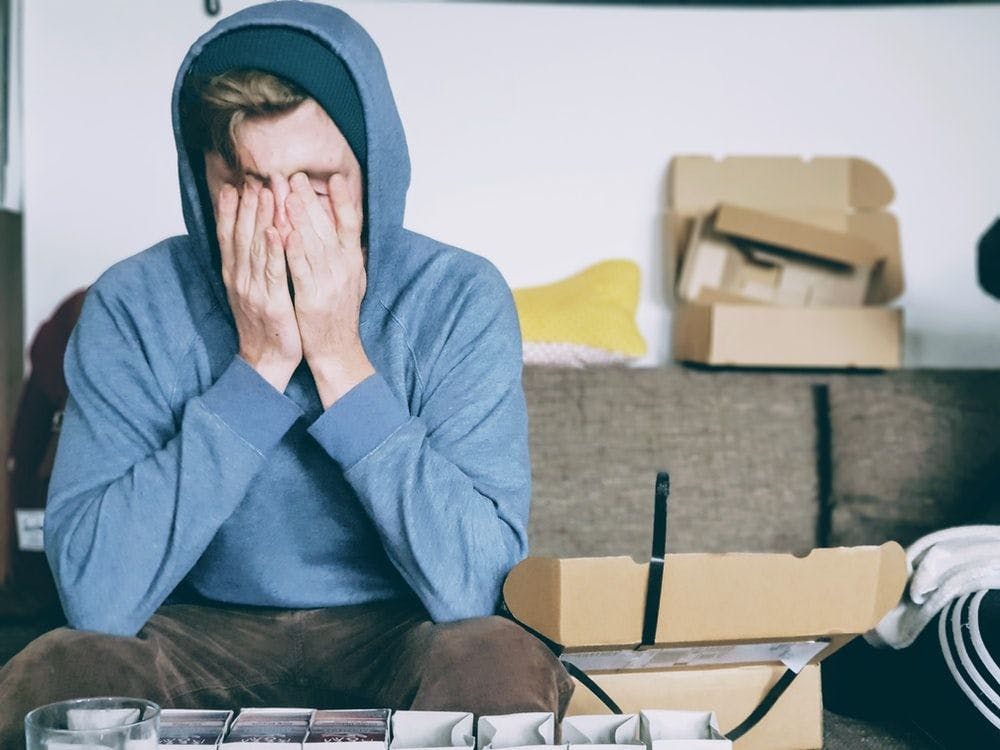 a teenage boy wearing a hoodie looks stressed with his hands over his face
