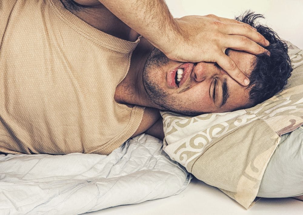 Man grabbing face while trying to sleep