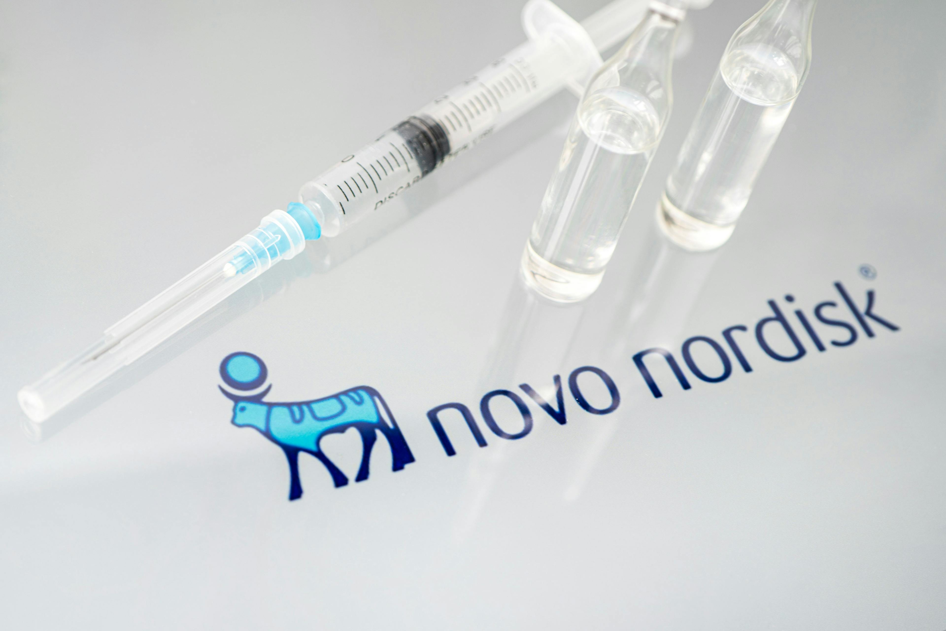 Vials of liquid on a white table and the logo of a large pharmaceutical company | Image credit: diy13 - stock.adobe.com