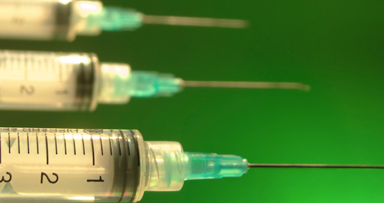 3 syringes front of a bright green background